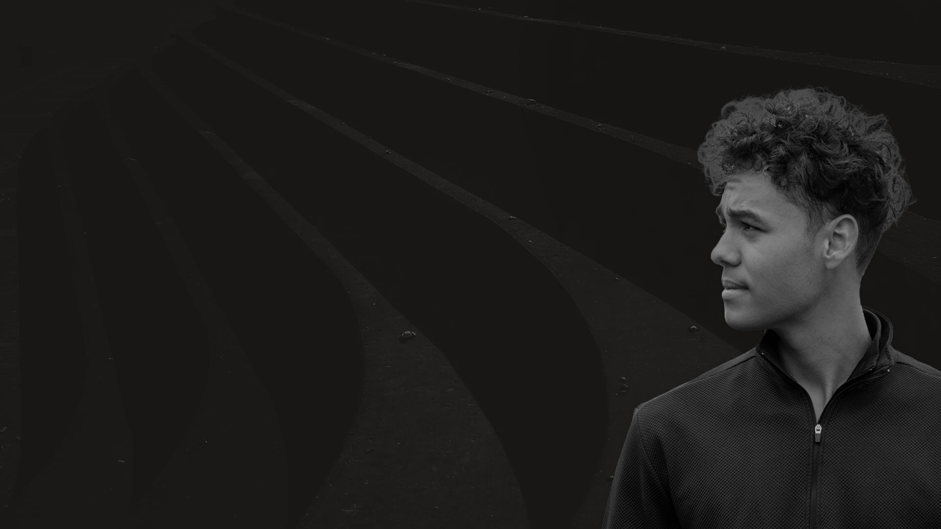 Aidan Renecke looking to the side in a black and white professional portrait, layered over a dark, abstract architectural background with sweeping curves.