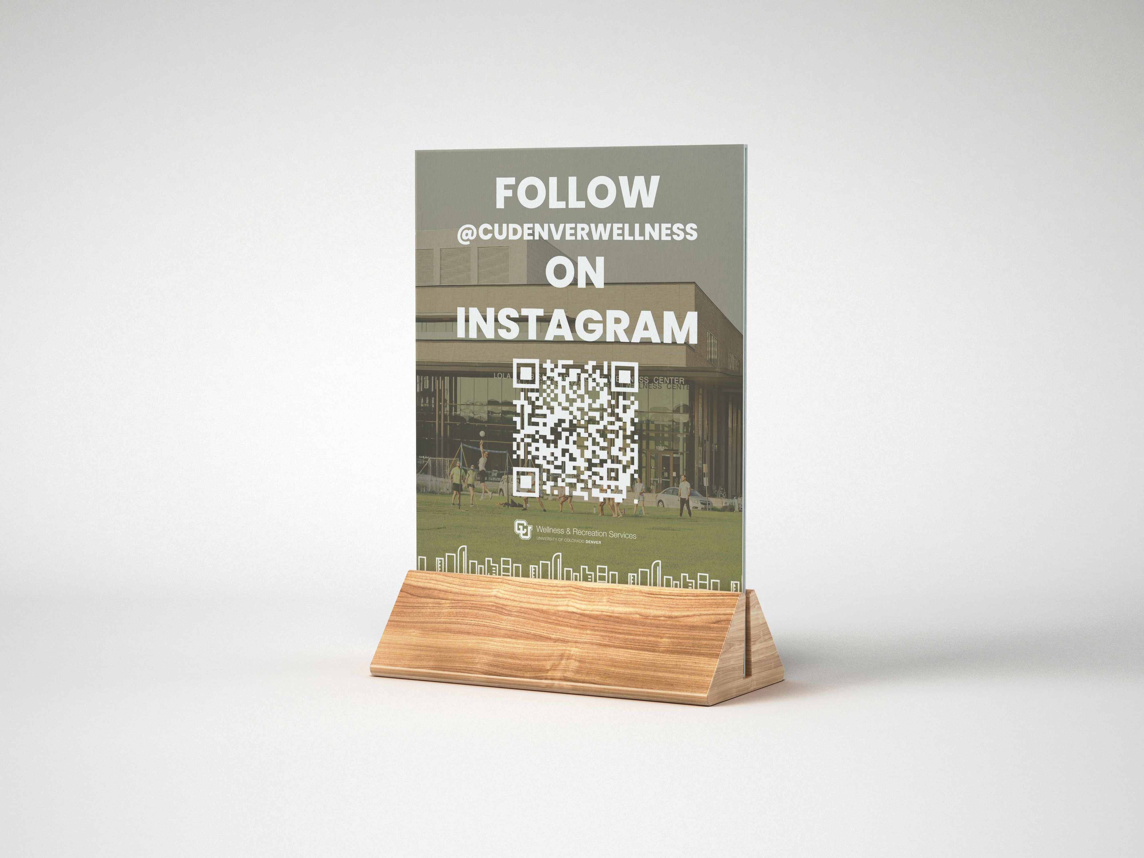 A desk mockup of a promotional acrylic stand featuring a QR code and an invitation to follow CU Denver Wellness on Instagram.