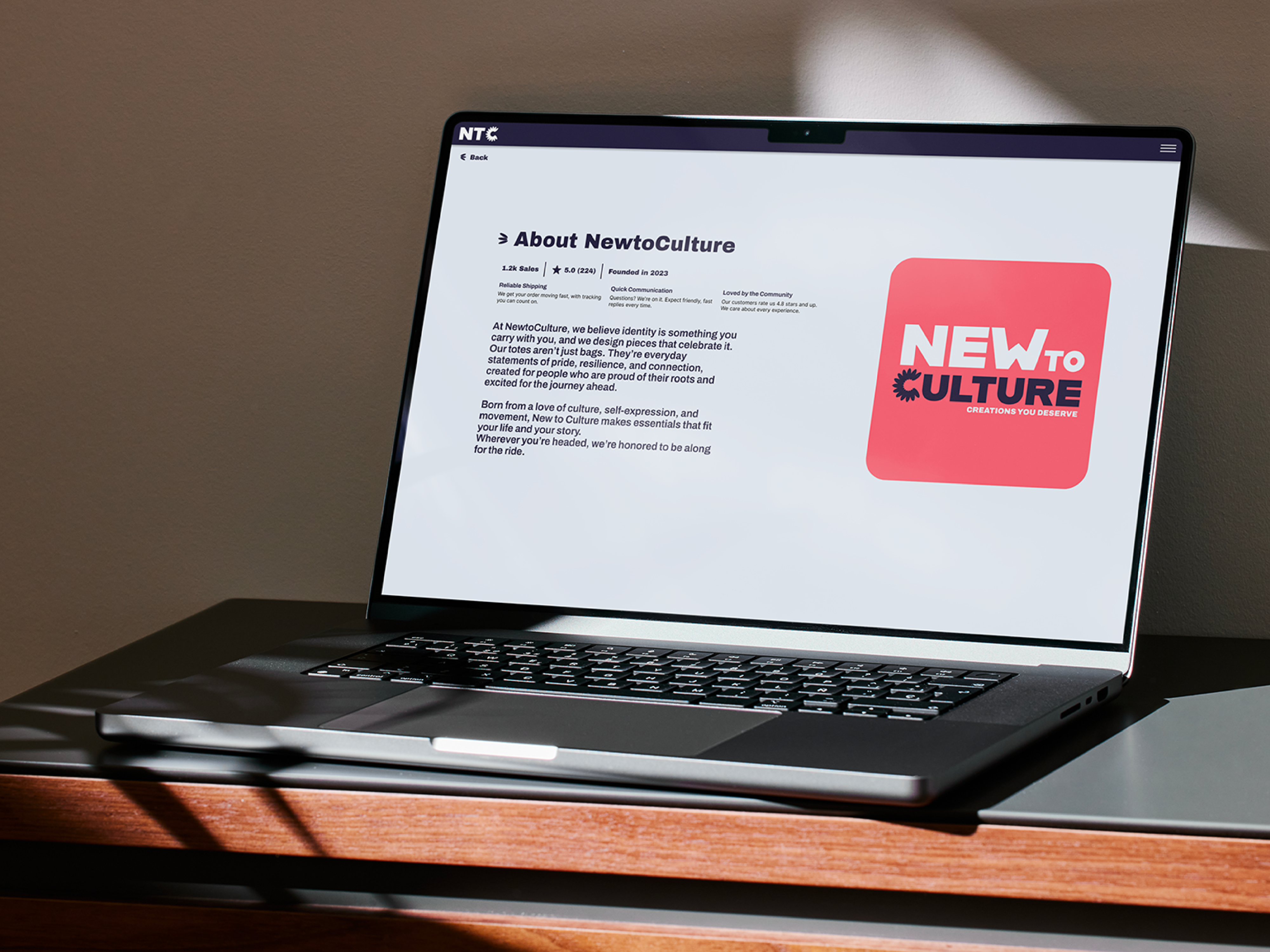 A MacBook Pro displaying the 'About NewToCulture' webpage, showcasing clean typography, brand storytelling, and the red square logo.