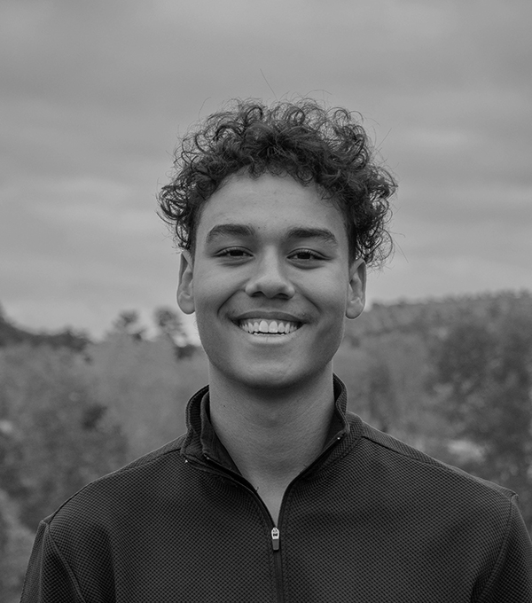 A smiling black and white headshot of Aidan Renecke against a blurred natural outdoor background.